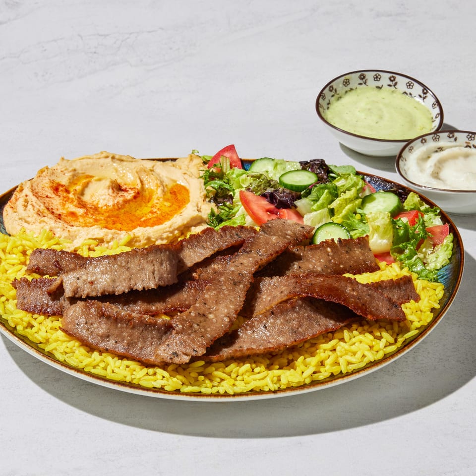 A platter of gyro meat, yellow rice, hummus, and a fresh garden salad with two dipping sauces.