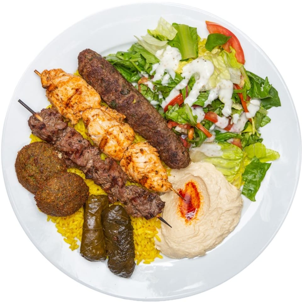 A Mediterranean platter with chicken and beef kebabs, falafel, stuffed grape leaves, rice, hummus, and salad.