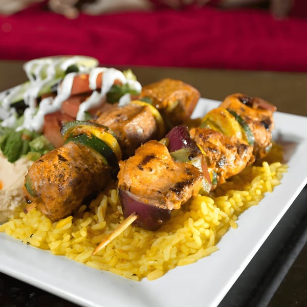 Chicken and vegetable skewers on a bed of yellow rice with a side salad.