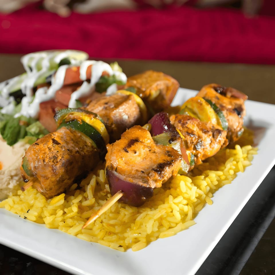 Chicken and vegetable skewers on a bed of yellow rice with a side salad.