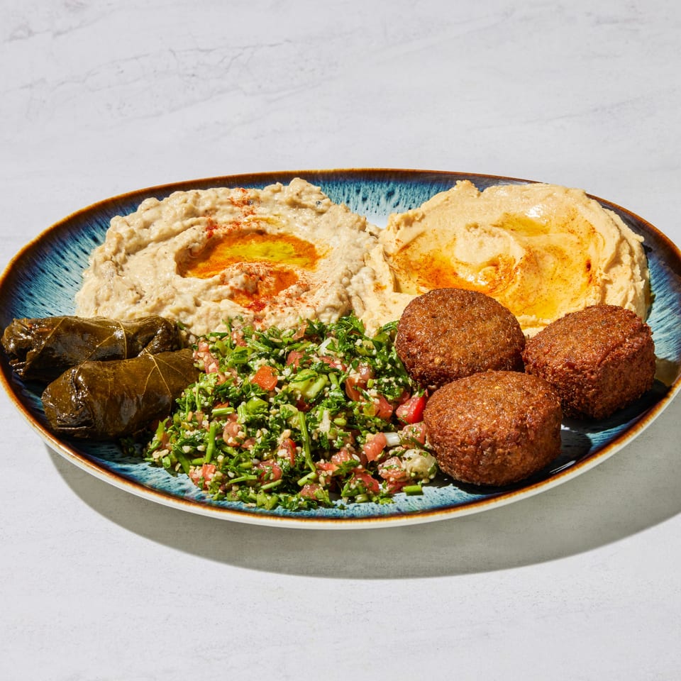 A blue plate with hummus, baba ghanoush, falafel, tabbouleh, and stuffed grape leaves.