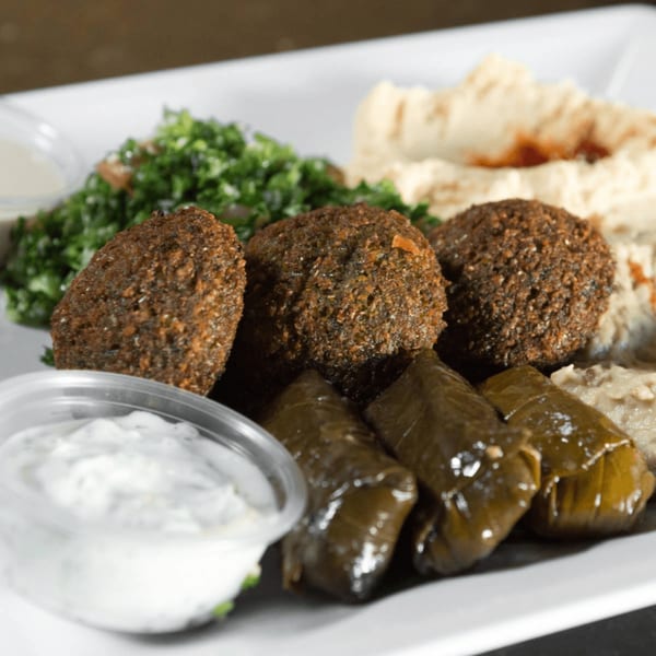 A Mediterranean platter with falafel, stuffed grape leaves, hummus, tabbouleh, and two dipping sauces.